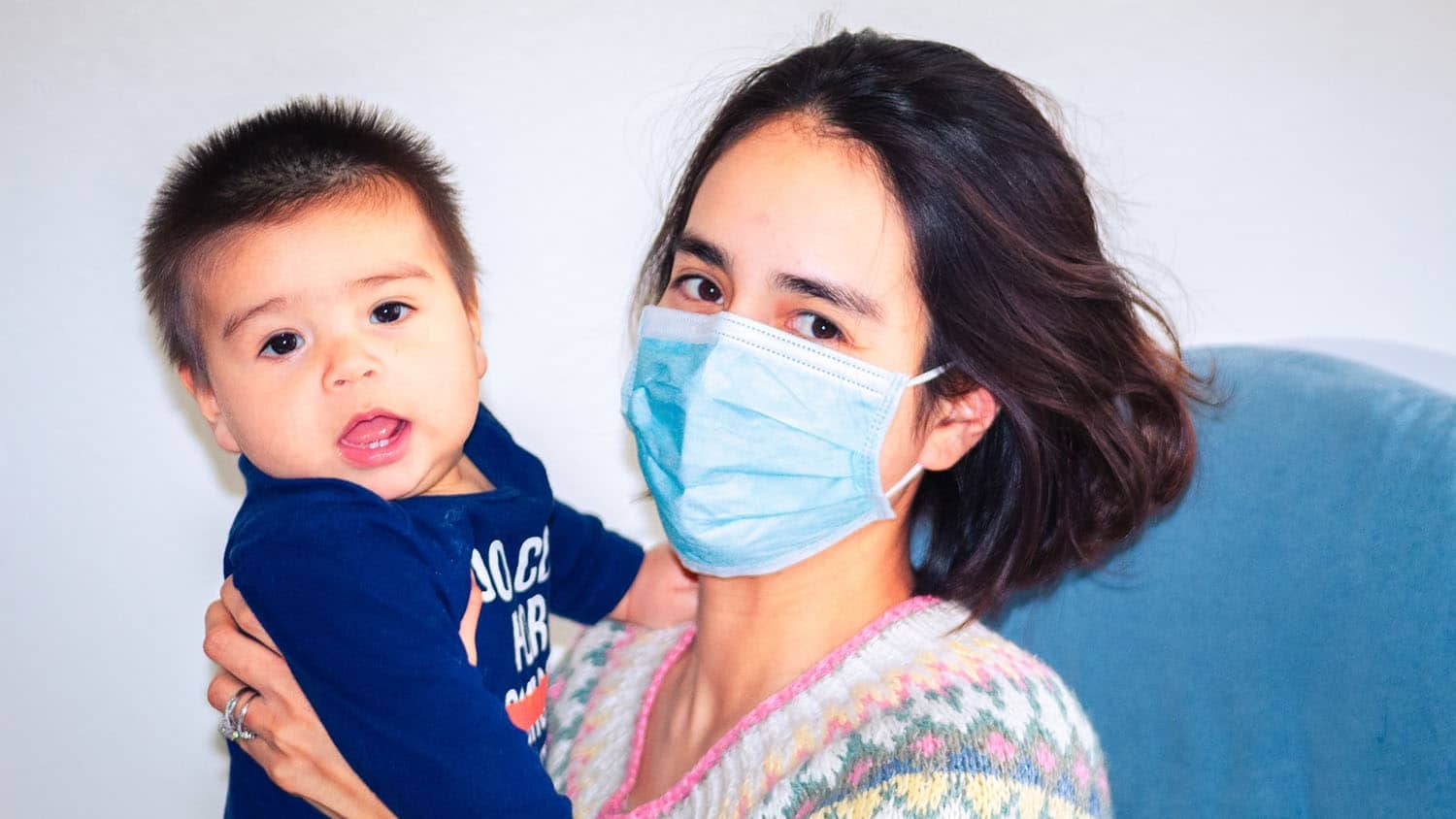 woman wearing a facemask holds an infant